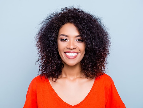 Woman with curly dark hair smiling at camera wearing bright red shirt against light blue background