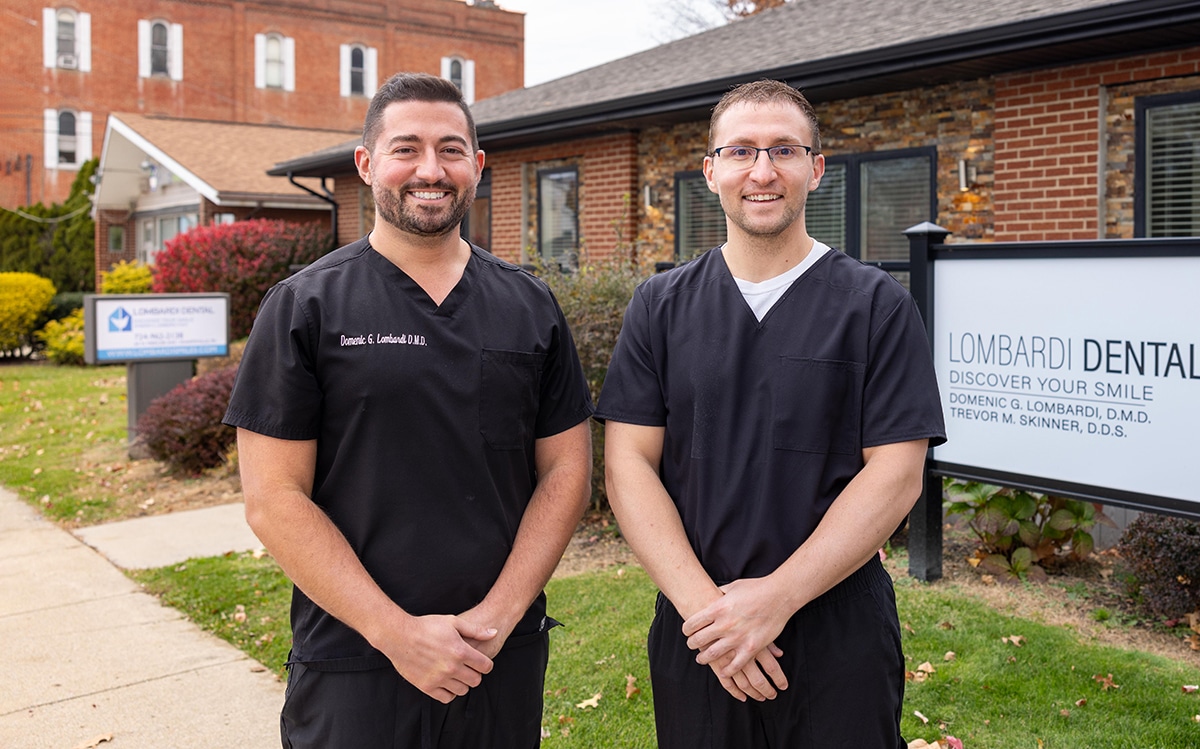 Two male dental professionals standing outside Lombardi Dental office building in scrubs.