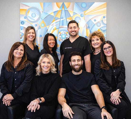 Lombardi Dental team of eight professionals in black attire posing together indoors with colorful artwork background.