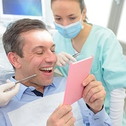 Dentist in mask shows smiling patient pink document in modern dental office setting.