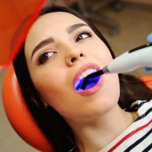 Woman receiving blue LED teeth whitening treatment at dental office