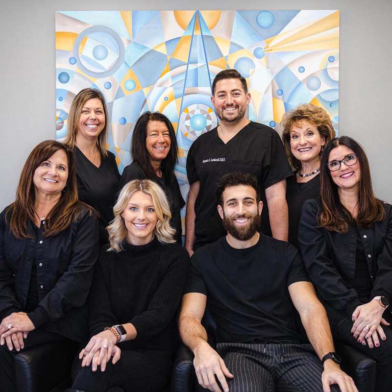 Lombardi Dental team of eight professionals posing together in front of colorful blue and gold artwork.