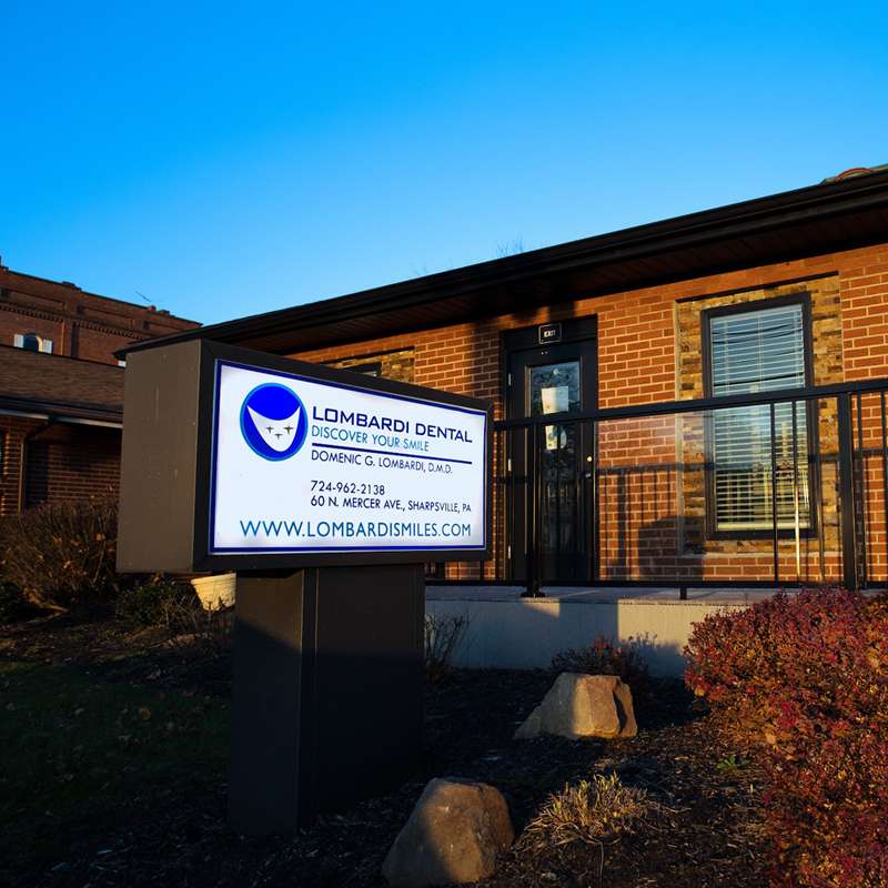 Lombardi Dental office exterior with illuminated sign at dusk, brick building entrance visible.